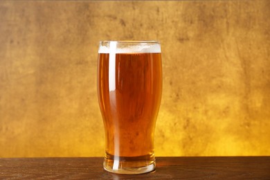 Glass with fresh beer on wooden table against yellow background