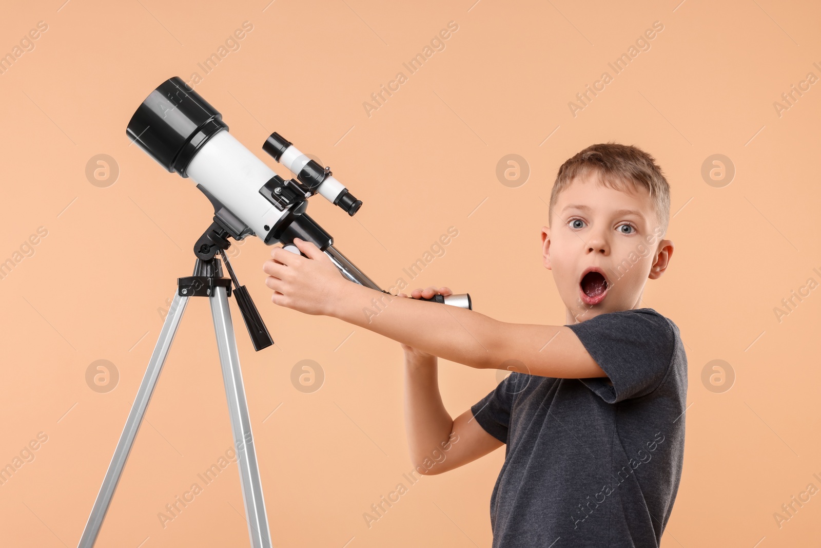 Photo of Surprised little boy with telescope on beige background