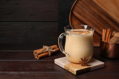 Photo of Delicious eggnog with spices on wooden table. Space for text