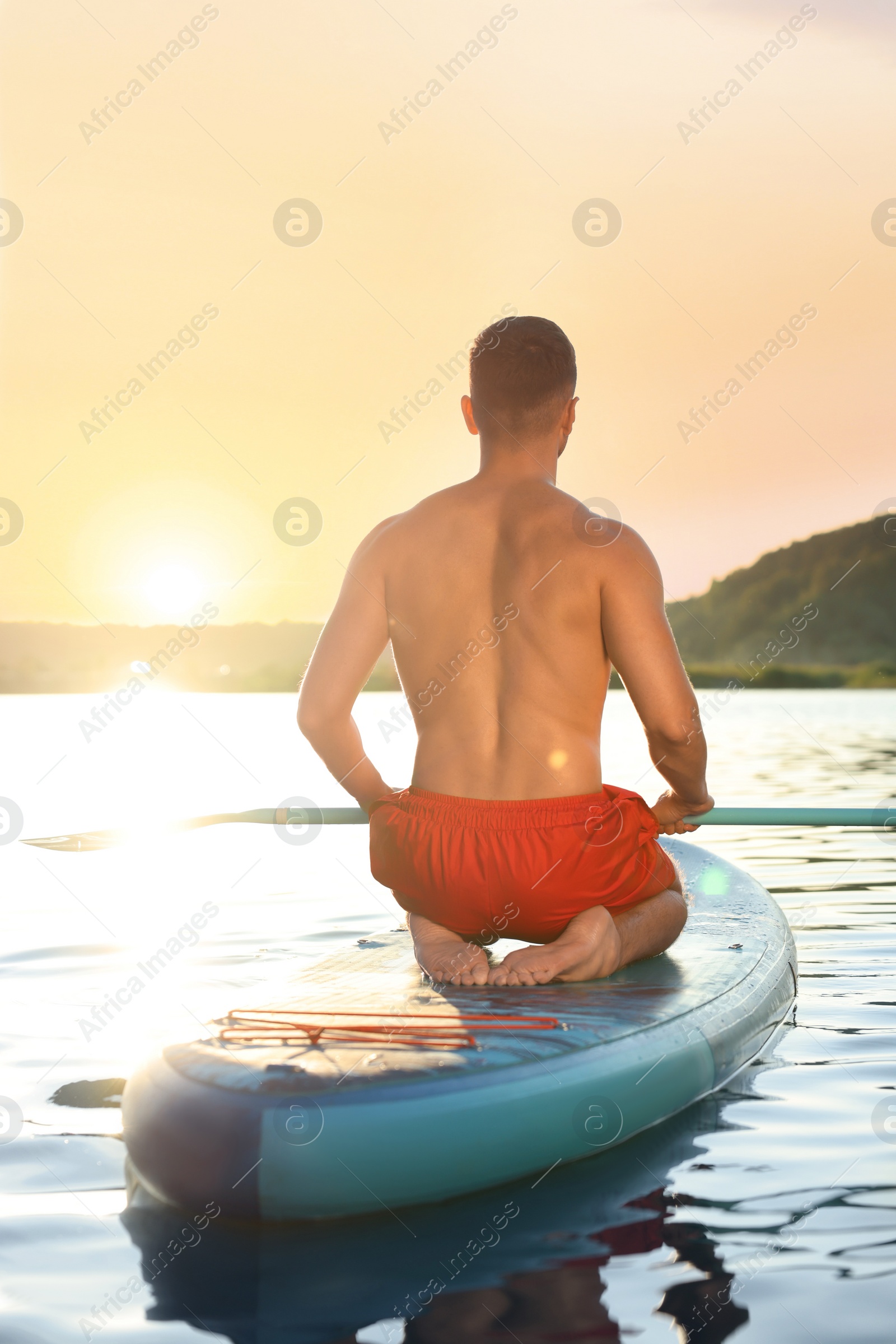 Photo of Man paddle boarding on SUP board in river at sunset, back view