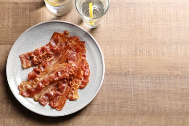 Plate with fried bacon on wooden background