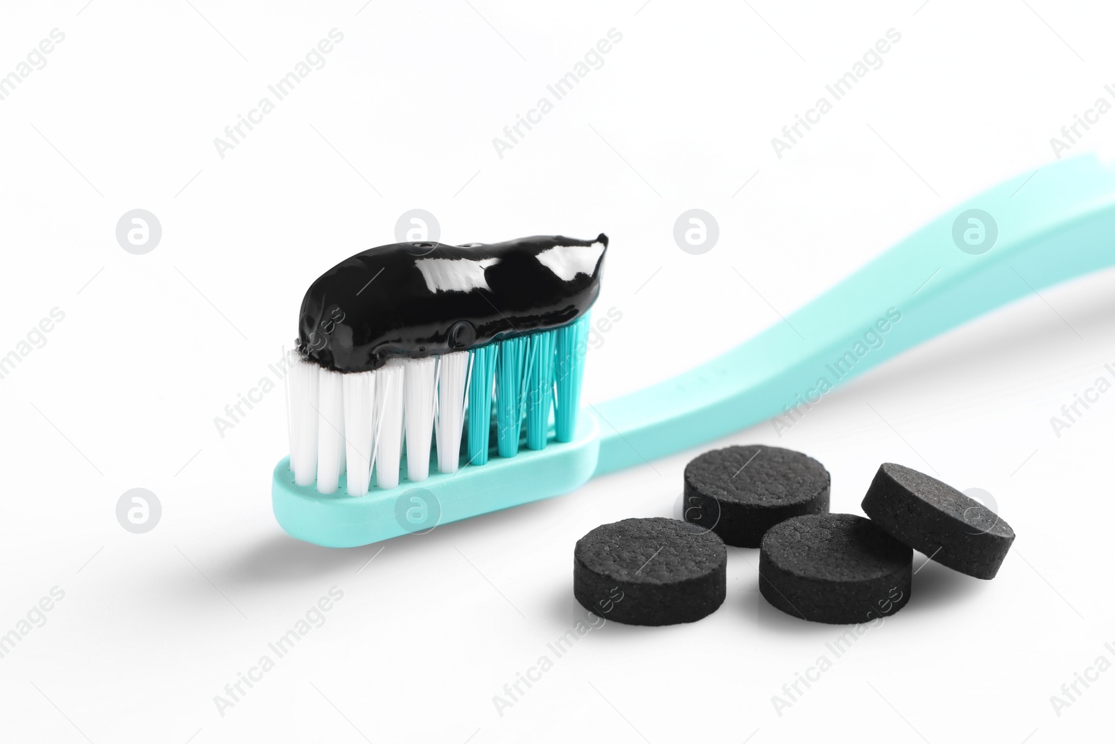 Photo of Brush with charcoal toothpaste and pills on white background