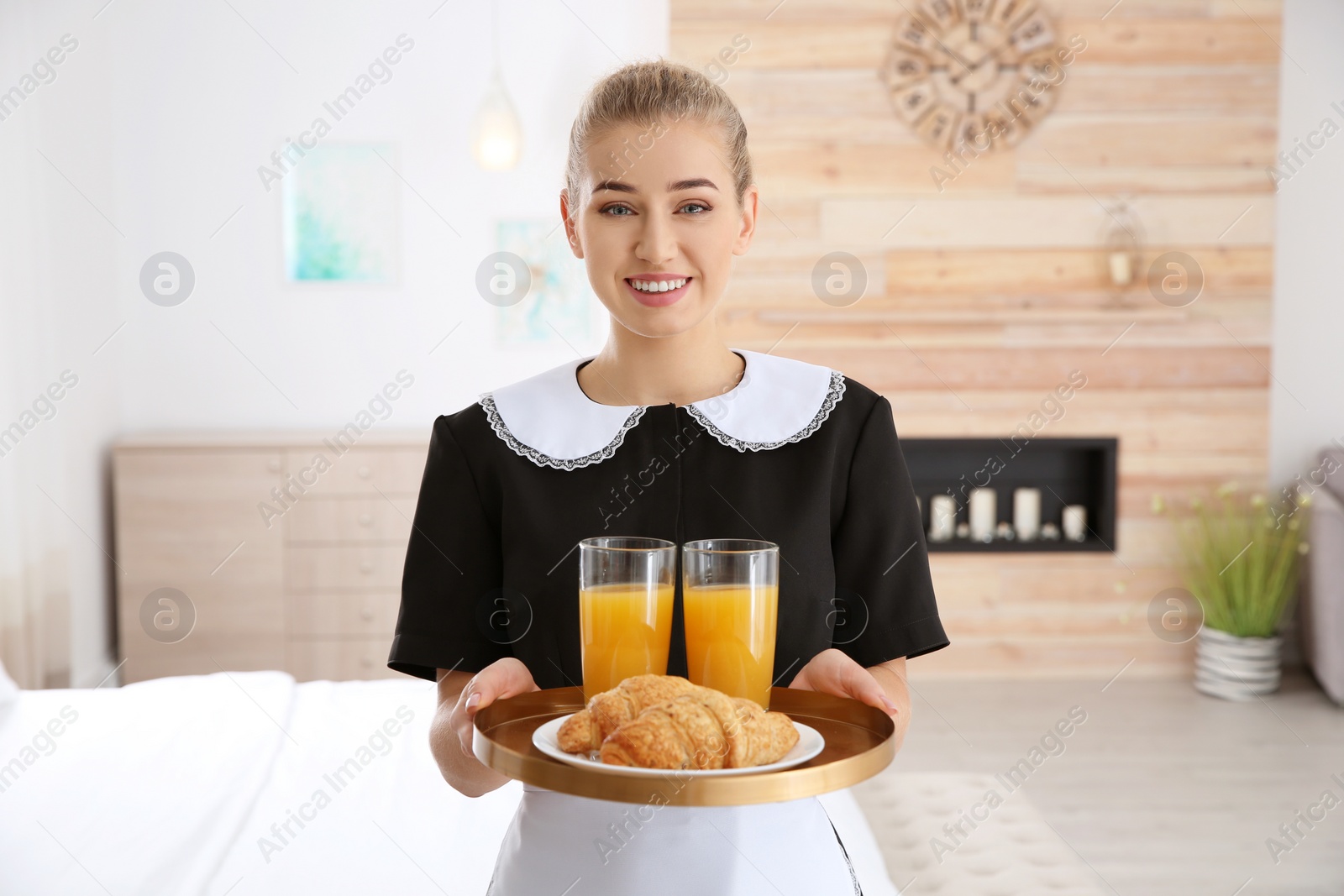 Photo of Young chambermaid holding tray with breakfast in hotel room