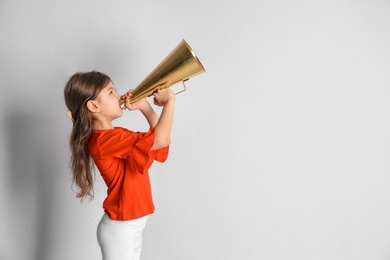 Photo of Adorable little girl with vintage megaphone on light background