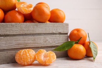 Delicious tangerines with leaves on light wooden table, closeup