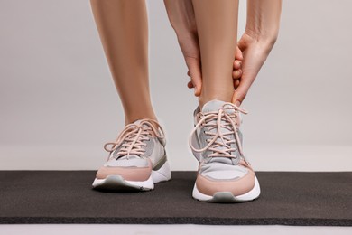 Photo of Woman suffering from leg pain on exercise mat against grey background, closeup