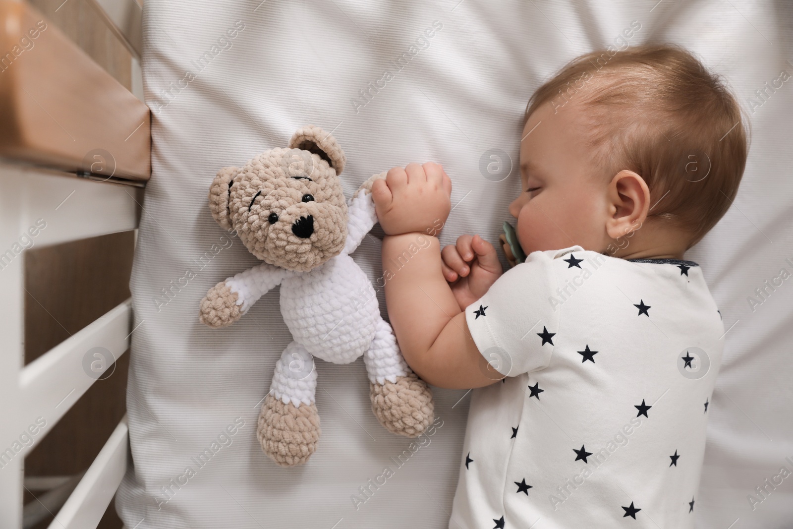 Photo of Adorable little baby with pacifier and toy sleeping in crib, top view