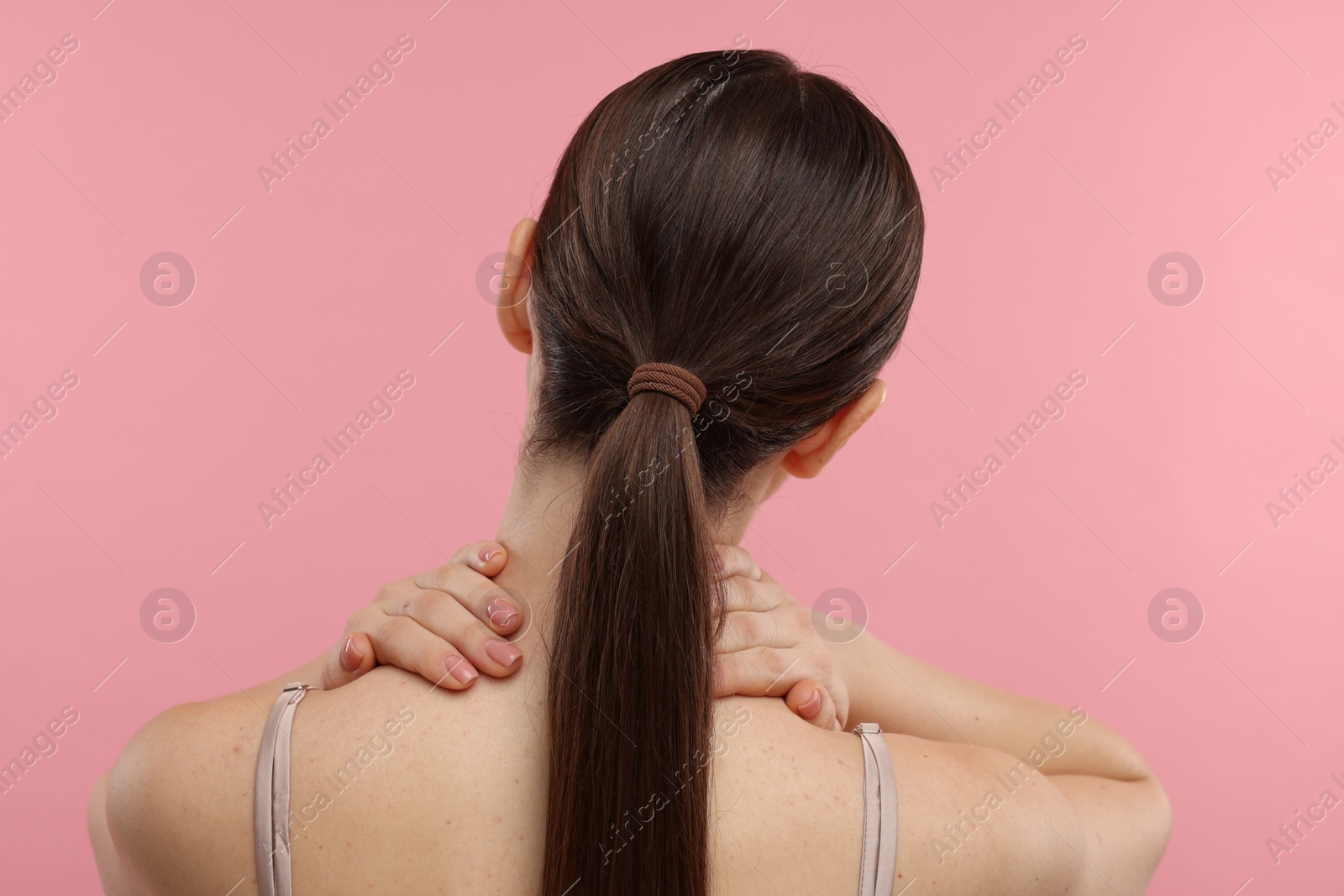 Photo of Woman touching her neck on pink background, back view