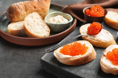 Photo of Delicious sandwiches with red caviar on wooden board