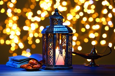 Photo of Arabic lantern, Quran, dates and Aladdin magic lamp on table against blurred lights at night