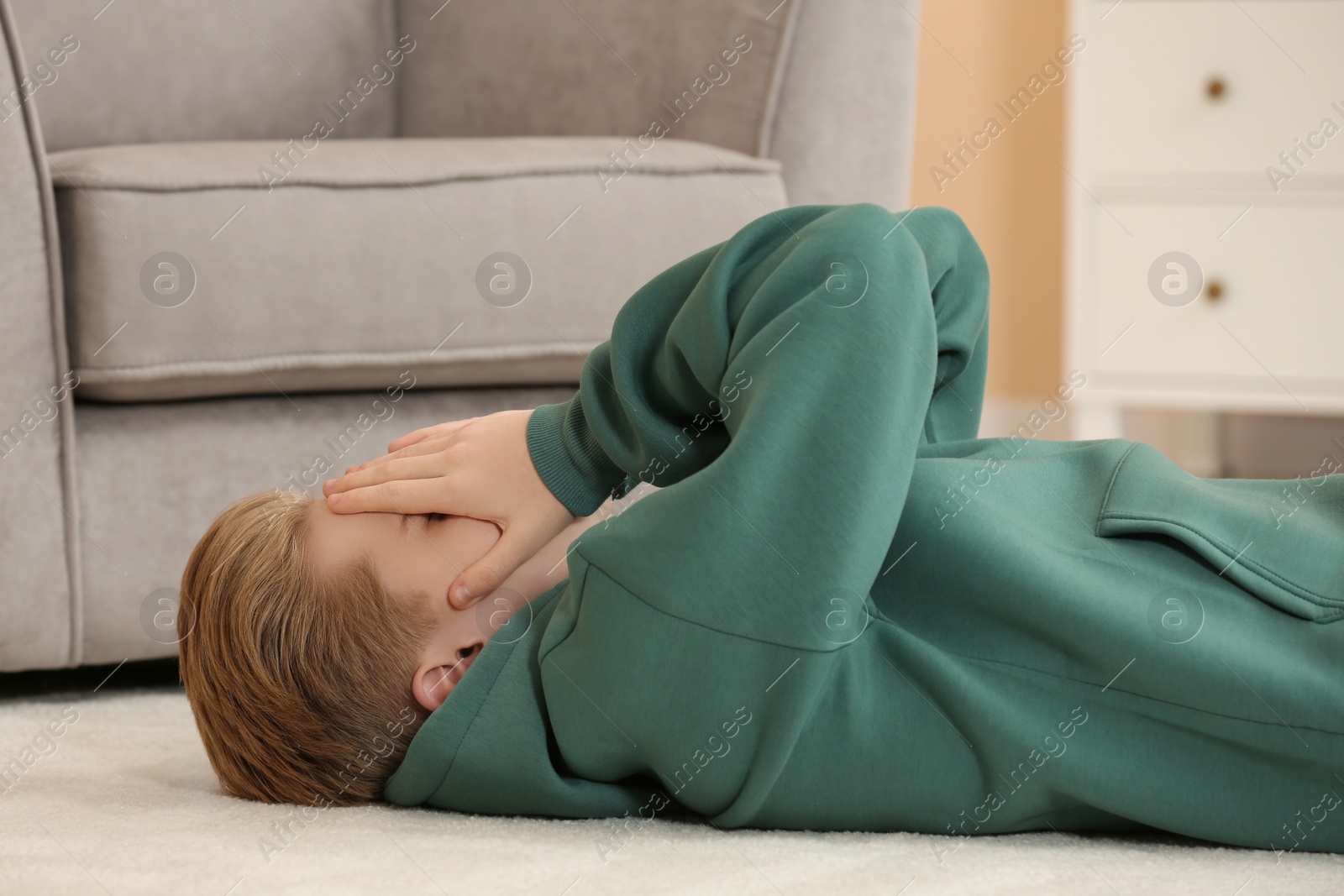 Photo of Unhappy teenage boy covering face with hands in room