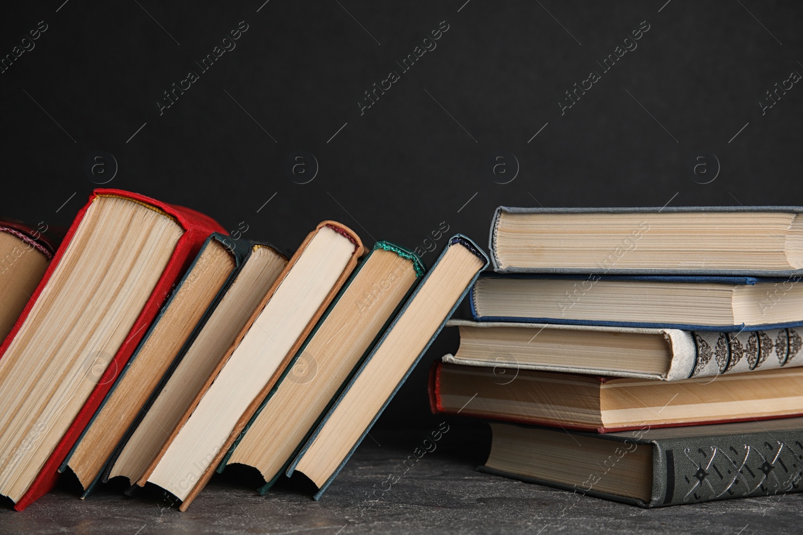 Photo of Stack of hardcover books on grey stone table against black background