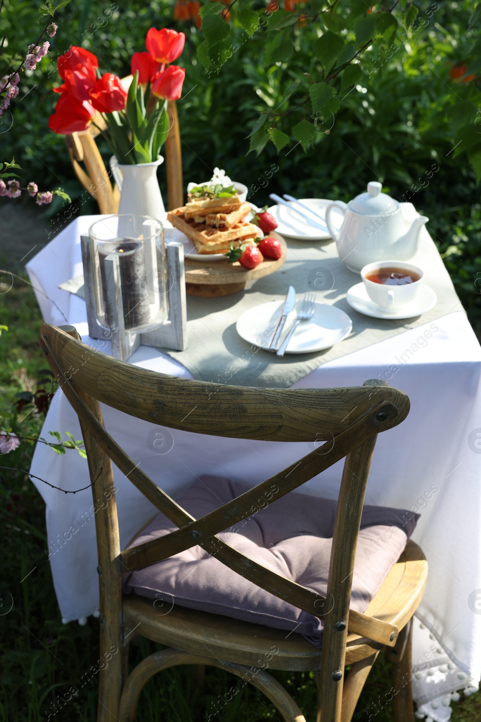 Photo of Beautiful bouquet of tulips and freshly baked waffles on table served for tea drinking in garden