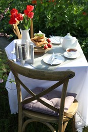 Photo of Beautiful bouquet of tulips and freshly baked waffles on table served for tea drinking in garden