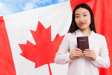 Immigration. Woman with passport and national flag of Canada against blue sky, space for text