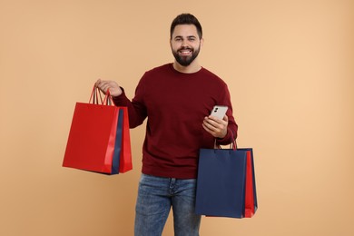 Photo of Smiling man with many paper shopping bags and smartphone on beige background