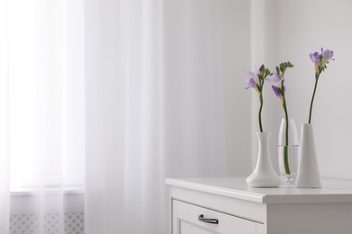 Photo of Beautiful spring freesia flowers on white chest of drawers in room, space for text