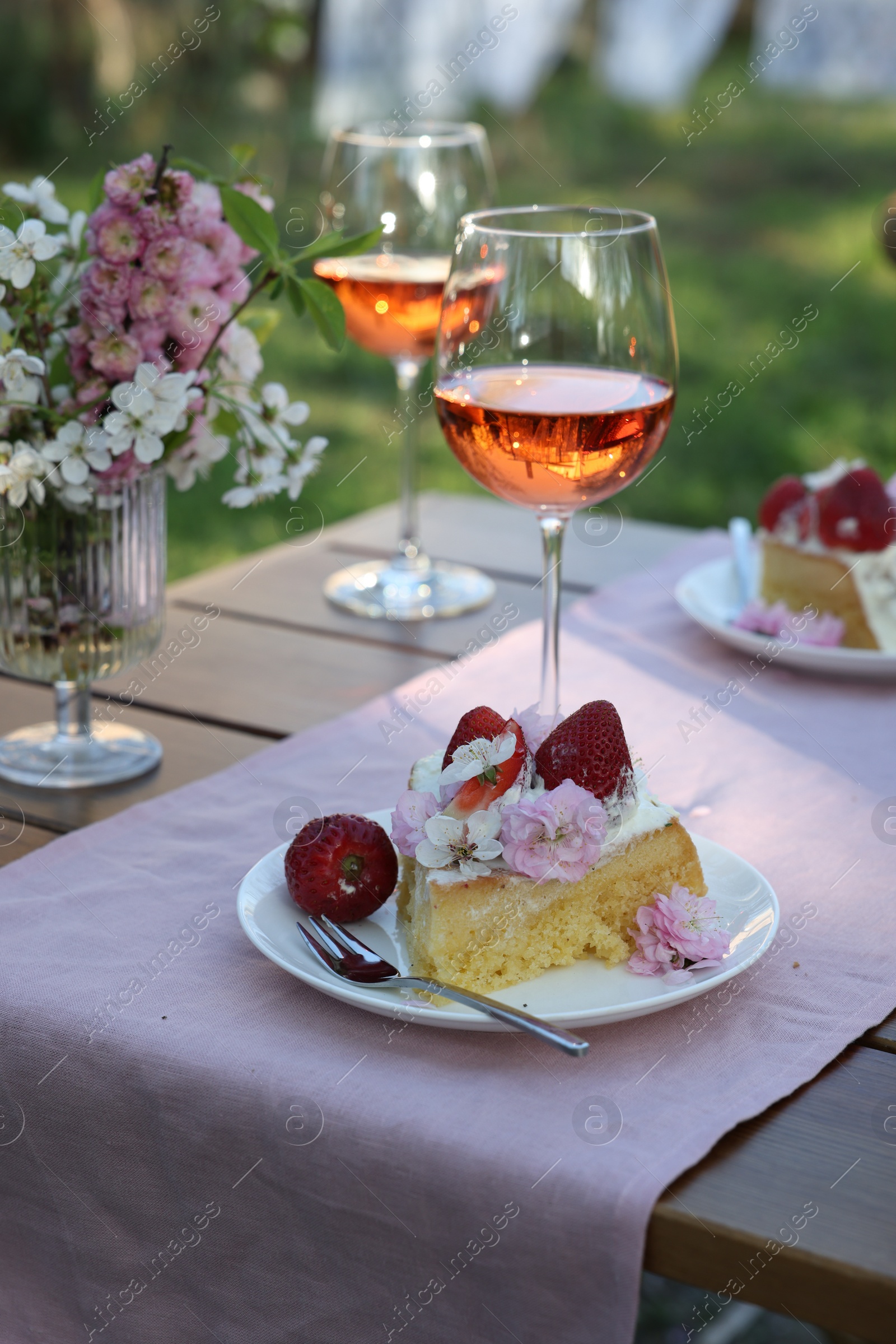 Photo of Vase with spring flowers, wine and cake on table served for romantic date in garden