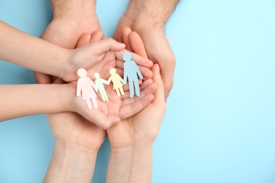 Parents and kid holding paper cutout of family in hands on turquoise background, top view. Space for text