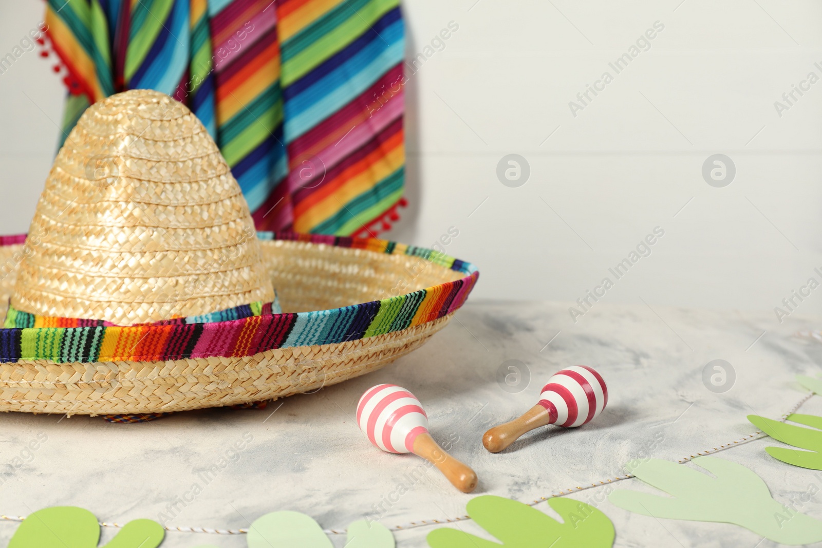 Photo of Mexican sombrero hat and maracas on grey textured table, closeup. Space for text
