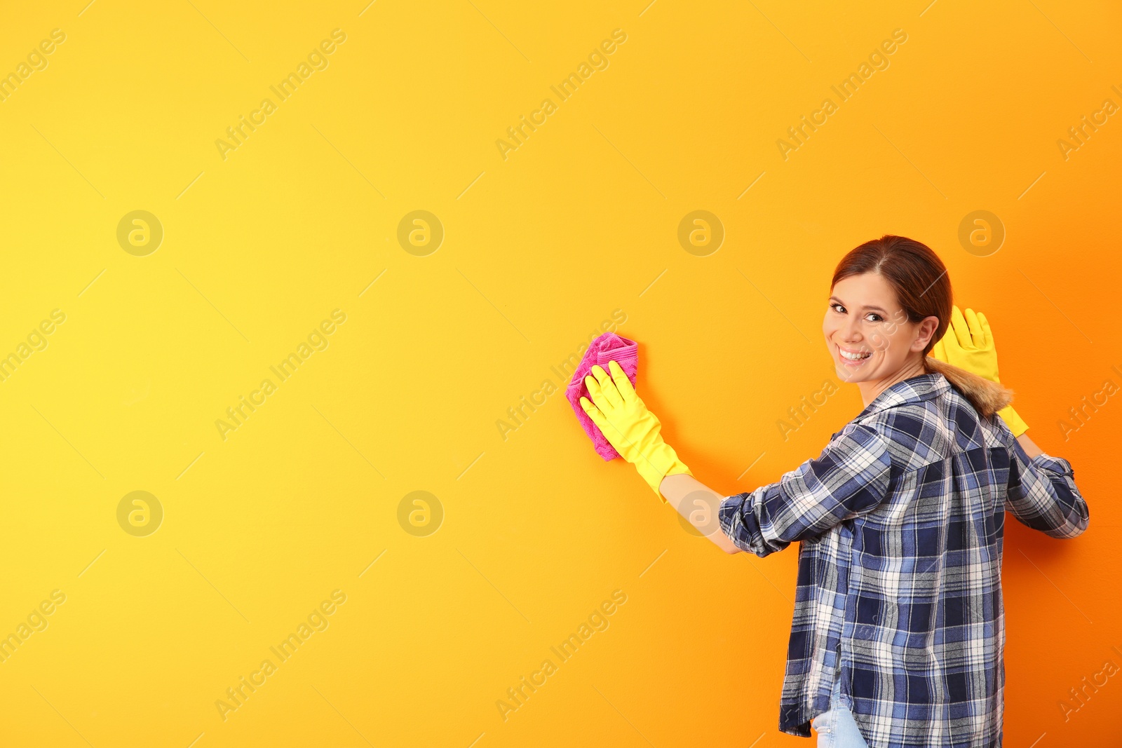 Photo of Young woman cleaning color wall with rag