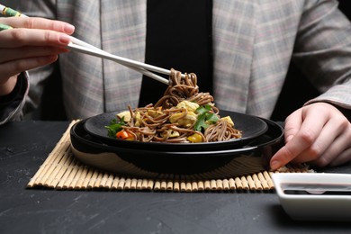 Photo of Stir-fry. Woman eating tasty noodles with meat and vegetables at dark textured table, closeup