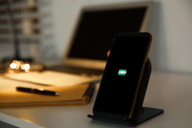 Photo of Mobile phone with wireless charger on table. Modern workplace accessory