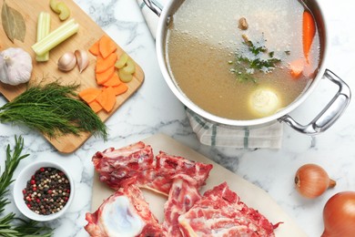 Photo of Delicious homemade bone broth and ingredients on white marble table, flat lay