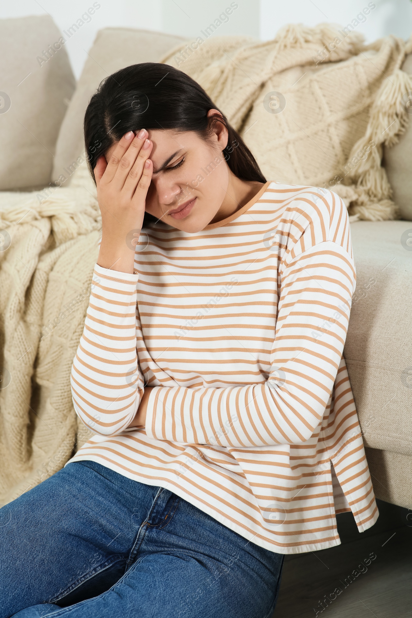 Photo of Young woman suffering from headache near sofa indoors. Hormonal disorders