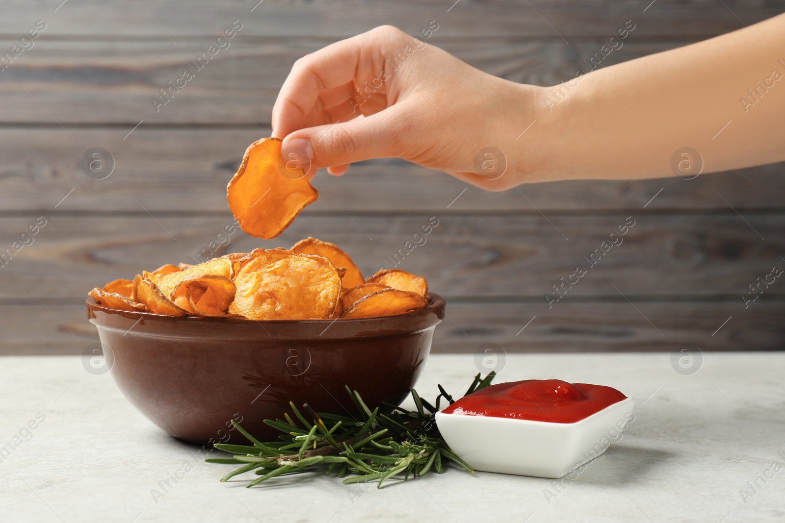 Photo of Woman taking sweet potato chip from bowl on table, closeup