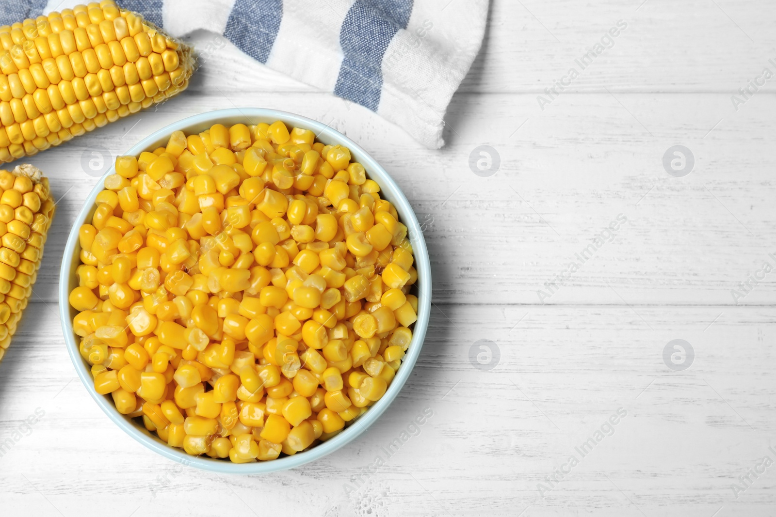 Photo of Delicious canned corn in bowl on white wooden table, flat lay. Space for text