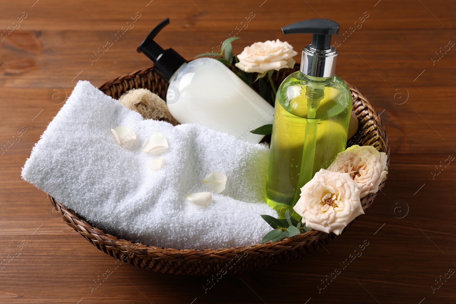 Photo of Dispensers of liquid soap, towel and roses in wicker basket on wooden table