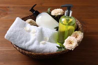 Dispensers of liquid soap, towel and roses in wicker basket on wooden table