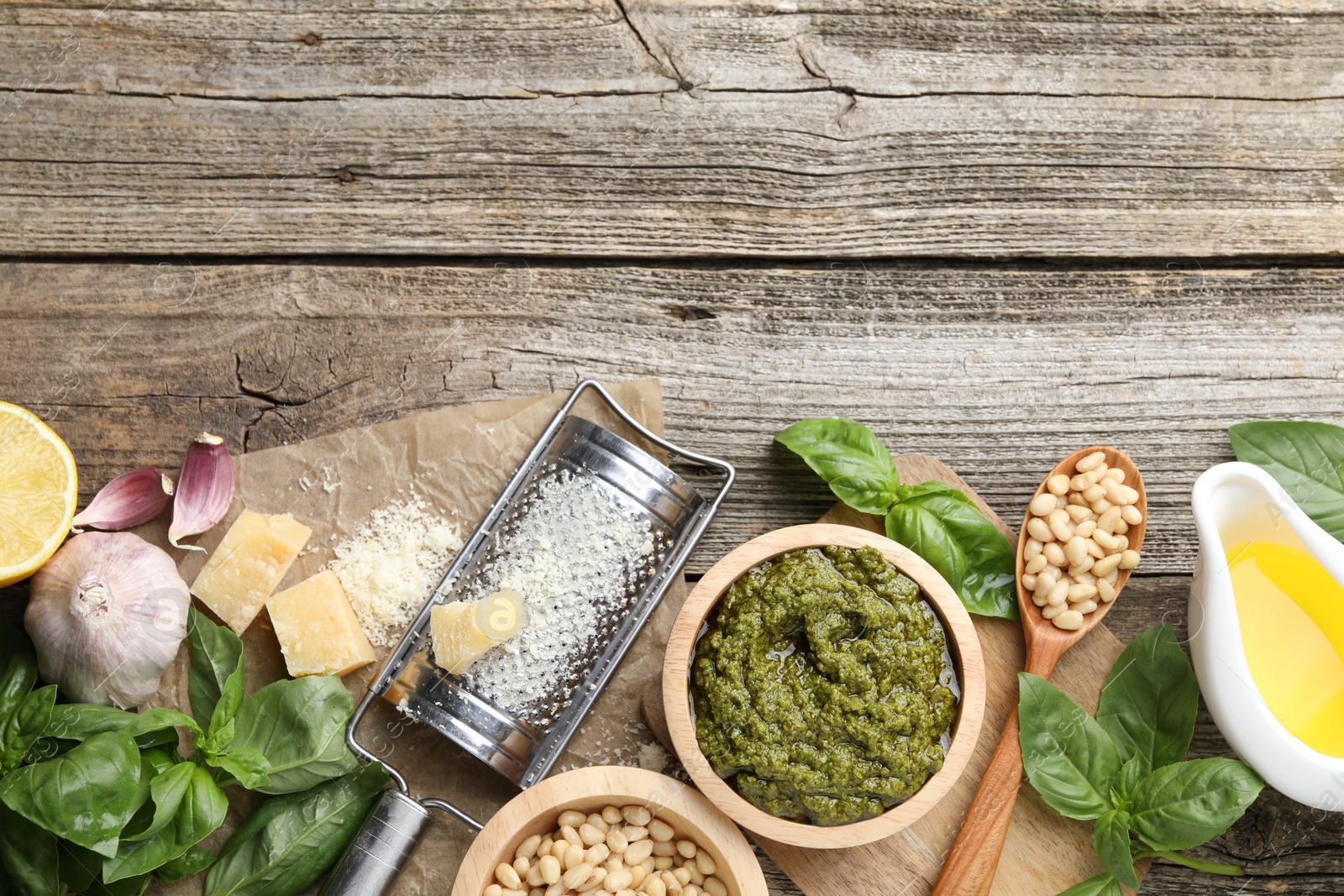 Photo of Tasty pesto sauce, basil, pine nuts, cheese, garlic and oil on wooden table, top view. Space for text