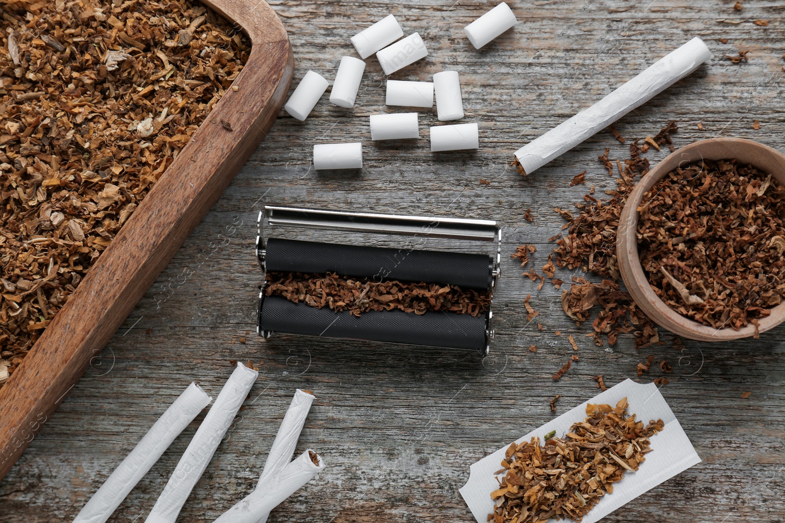 Photo of Flat lay composition with roller and tobacco on old wooden table. Making hand rolled cigarettes