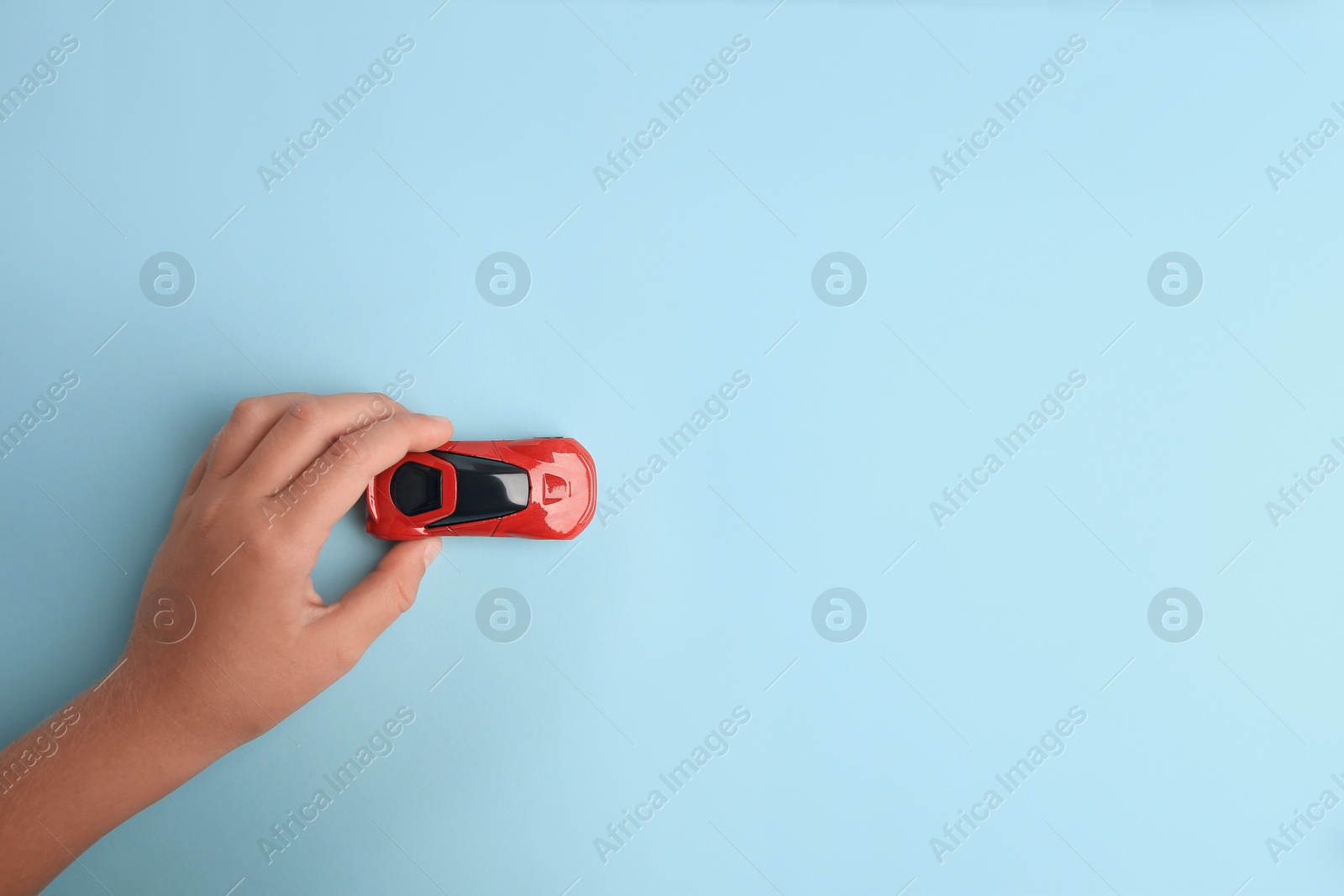 Photo of Child playing with toy car on light blue background, top view. Space for text