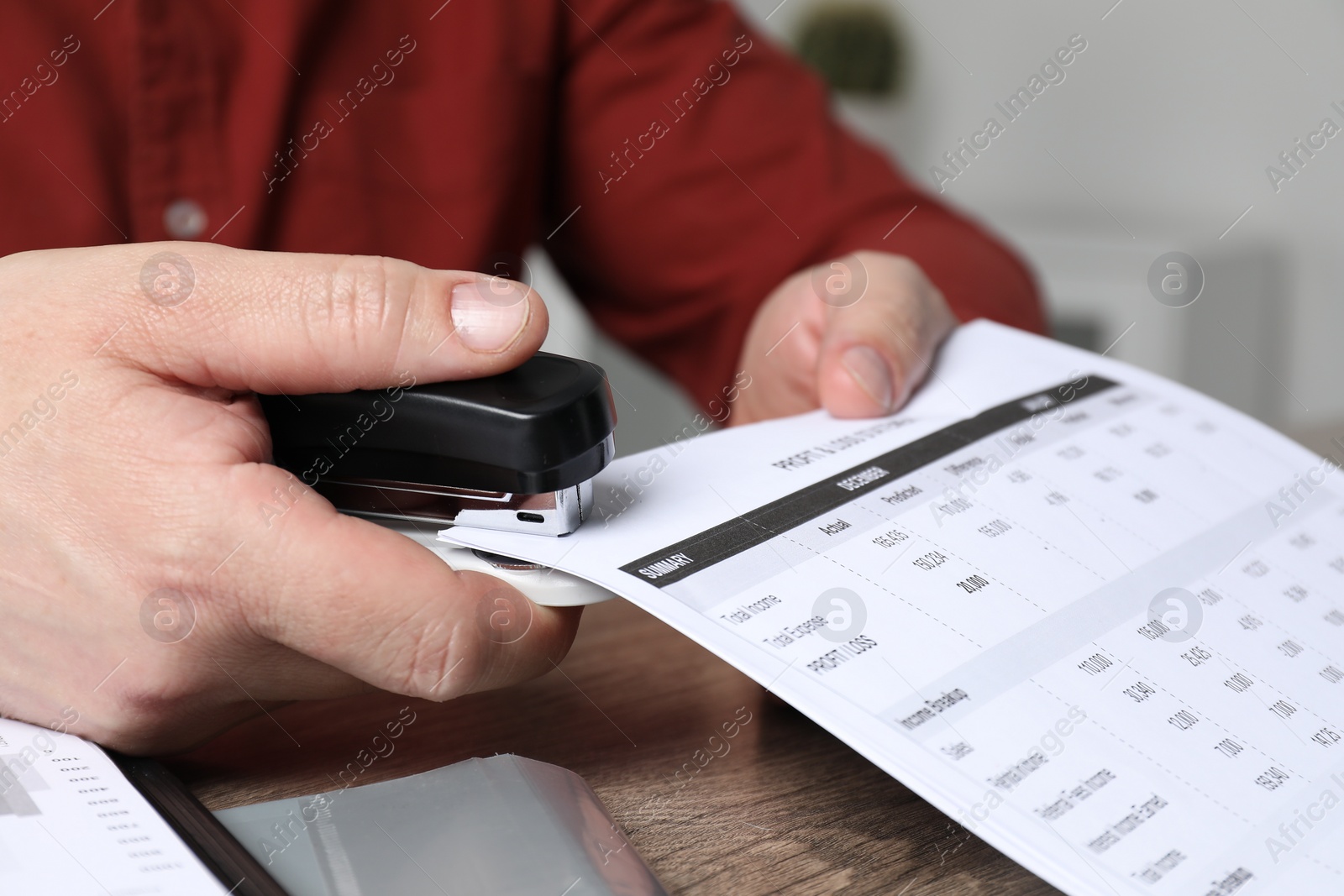 Photo of Man with documents using stapler at wooden table, closeup