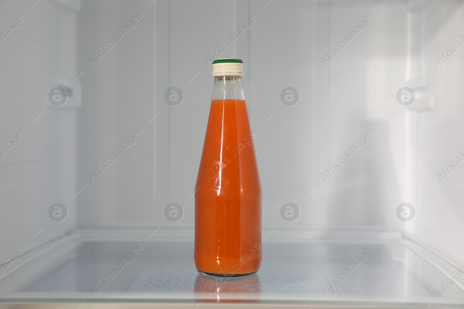 Photo of Bottle of juice on shelf inside modern refrigerator