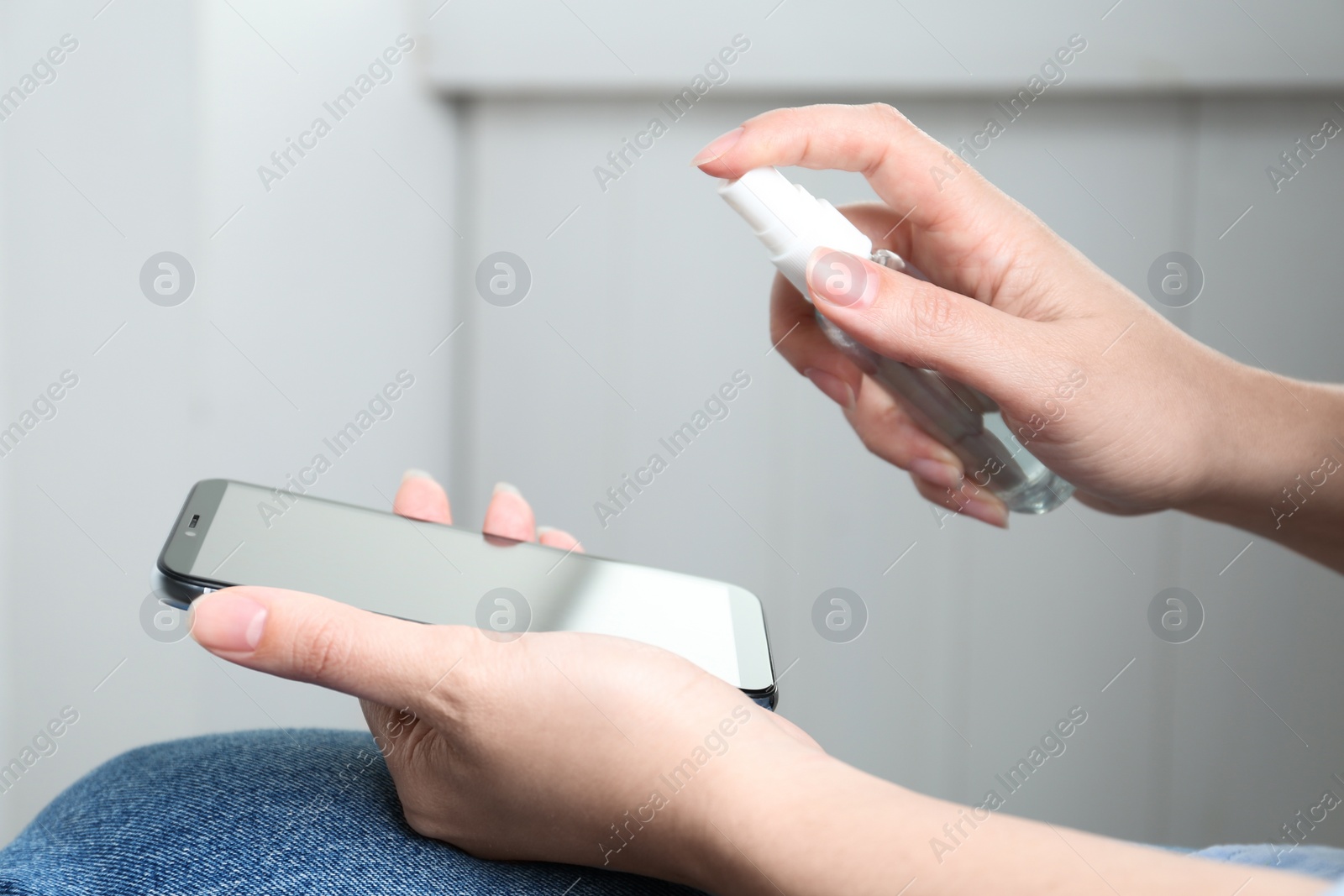 Photo of Woman spraying antiseptic onto smartphone indoors, closeup