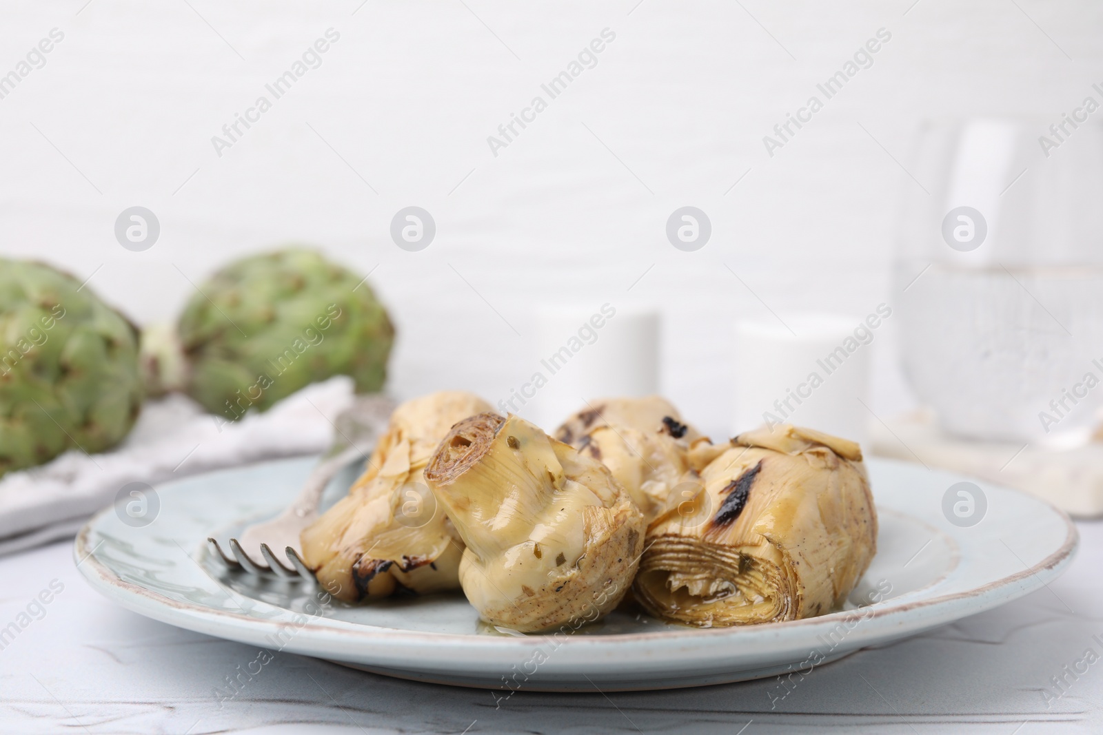 Photo of Delicious pickled artichokes served on white textured table, closeup