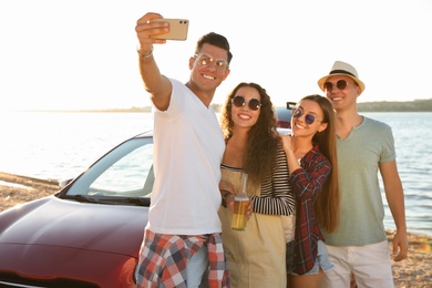 Photo of Happy friends taking selfie near car on beach. Summer trip
