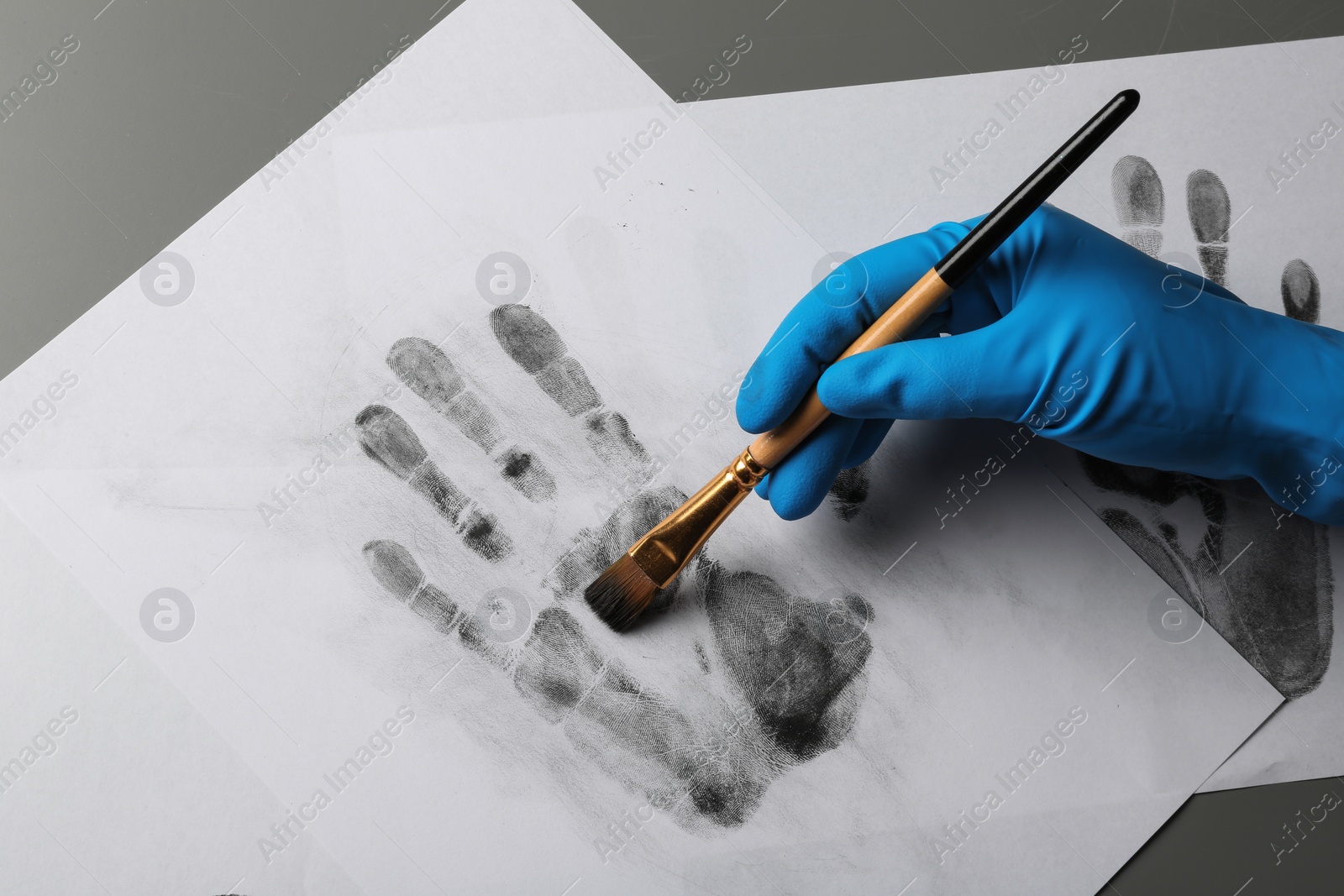 Photo of Detective taking fingerprints with brush from paper on grey background, top view.  Criminal investigation