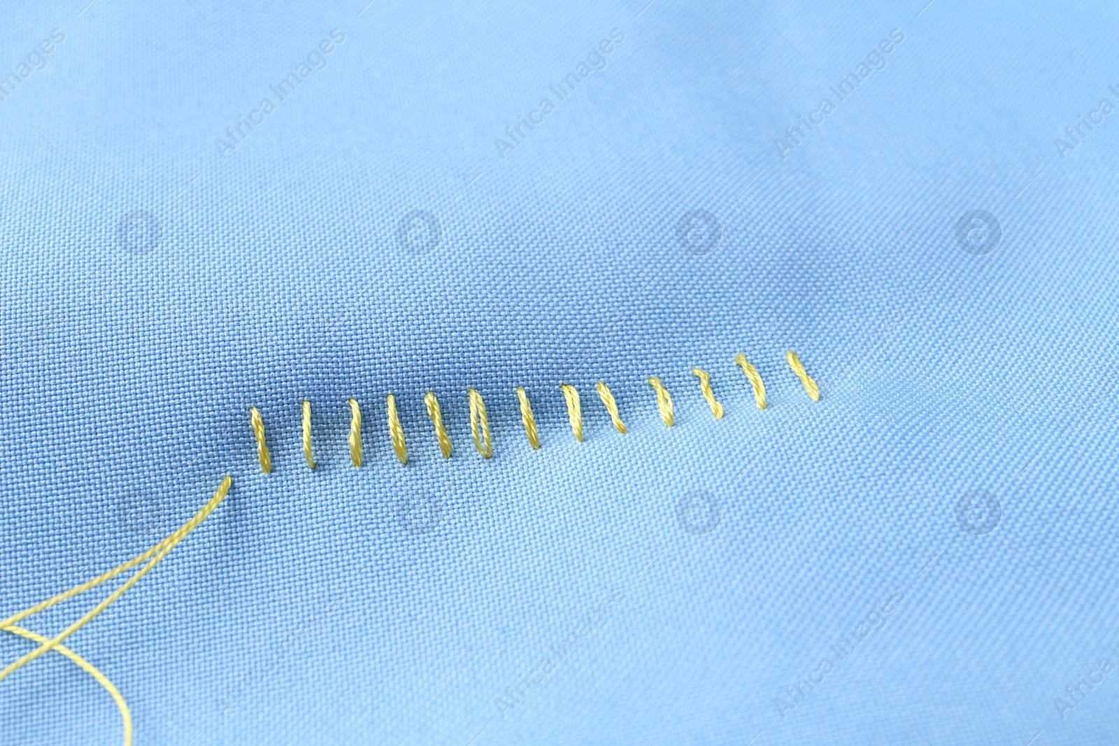 Photo of Sewing thread and stitches on light blue cloth, above view