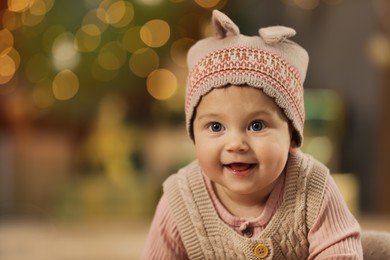 Photo of Cute little baby and blurred Christmas lights on background, space for text. Winter holiday