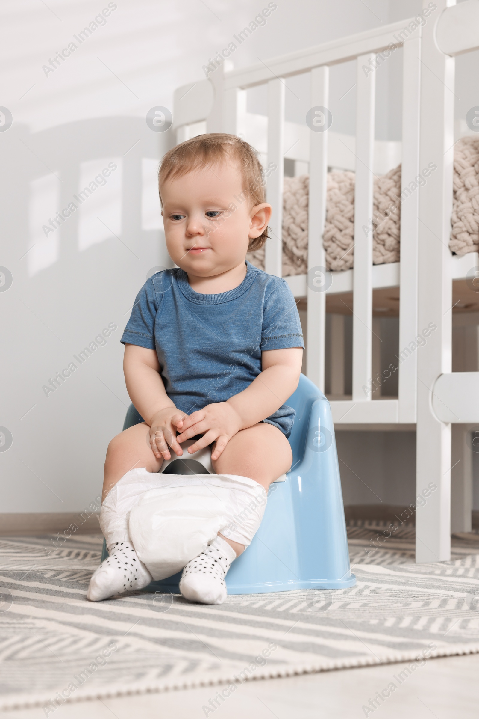 Photo of Little child sitting on plastic baby potty indoors