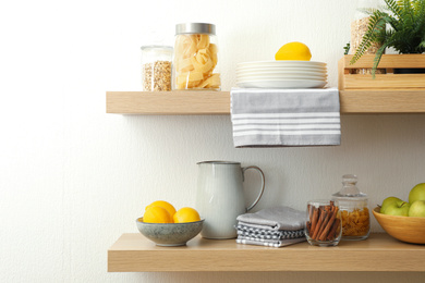 Wooden shelves with dishware and products on white wall. Kitchen interior idea