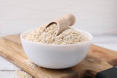 Photo of Raw barley groats and scoop in bowl on white wooden table, closeup