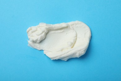 Photo of Smear of delicious cream cheese on light blue background, top view