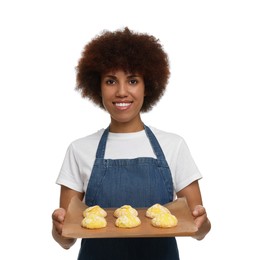 Happy young woman in apron holding board with cookies on white background