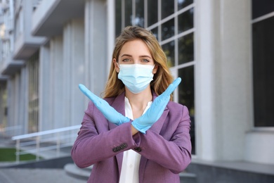 Woman in protective face mask showing stop gesture outdoors. Prevent spreading of coronavirus